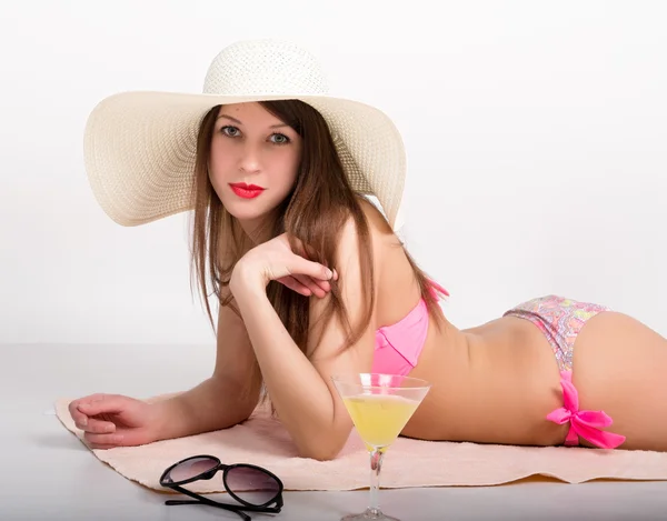 Bella ragazza in bikini, occhiali da sole e un grande cappello sdraiato sul telo mare in piedi accanto a un bicchiere di cocktail — Foto Stock