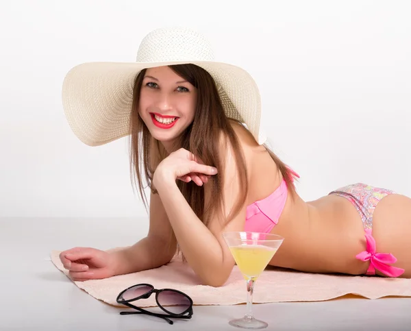 Menina bonita em biquíni, óculos de sol e um grande chapéu deitado na toalha de praia ao lado de um copo de coquetel — Fotografia de Stock
