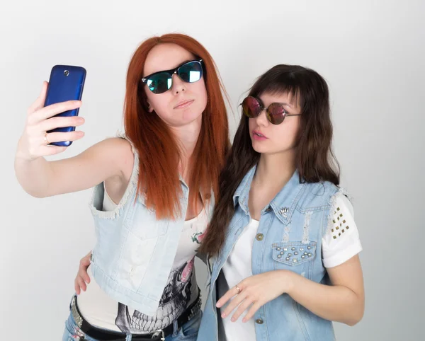 Krásy hipsterové dívky černé a červené v slunečních brýlích, dělají si z telefonu selu. Teenageři grimasa — Stock fotografie