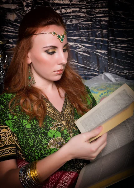 Closeup of Beautiful woman dressed in oriental style with oriental patterns on the hands and face, reading a thick book