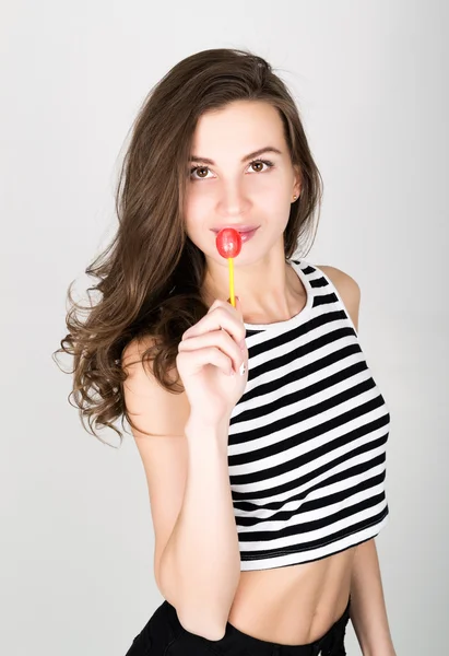 Mooi slank meisje in zwarte korte broek en een gestreepte top, eten van snoep. Closeup lip likken snoep — Stockfoto