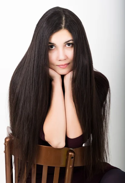 Schöne asiatische junge Brünette in einem dunklen Kleid sitzt auf einem Stuhl — Stockfoto