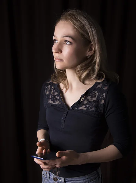 Szép lány, kezében egy telefon a kezében egy sötét háttér — Stock Fotó