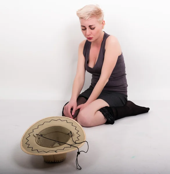 Részeg szőke nő ül a padlón, zoknit húzta le előtte egy kalap — Stock Fotó