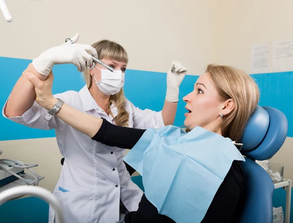 Доктор вивчає порожнину рота при розпаді зуба. Захист від карієсу. Лікування розпаду зубів. Лікар ставить ін'єкцію пацієнту, пацієнт тримає лікарів за руку і не ставить постріл — стокове фото