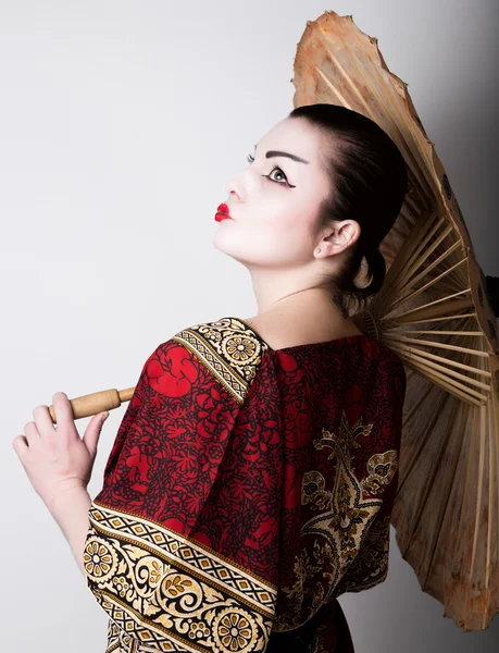 Vacker flicka klädd som en geisha girl innehar en kinesisk paraply. Geisha makeup och hår klädd i en kimono. Begreppet traditionella japanska värden — Stockfoto