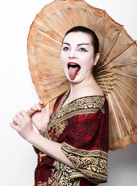 Hermosa chica vestida como una chica geisha sosteniendo un paraguas chino. Maquillaje geisha y pelo vestido con un kimono. El concepto de valores tradicionales japoneses — Foto de Stock