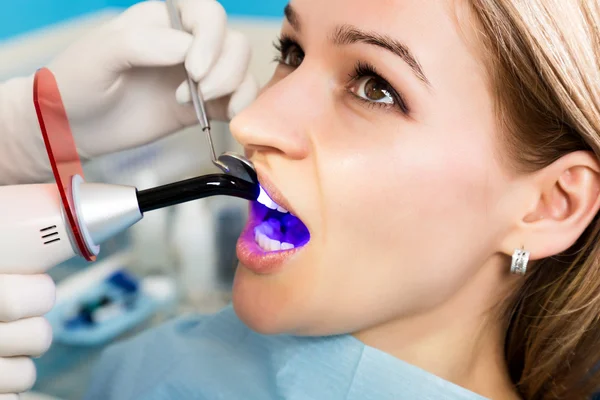 The reception was at the female dentist. Doctor examines the oral cavity on tooth decay. Caries protection. Tooth decay treatment. Dentist working with dental polymerization lamp in oral cavity — Stock Photo, Image