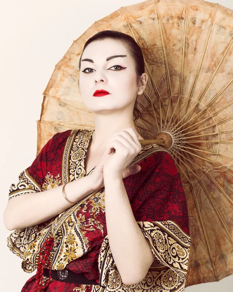 Beautiful girl dressed as a geisha girl holding a Chinese umbrella. Geisha makeup and hair dressed in a kimono. The concept of traditional Japanese values — Stock Photo, Image