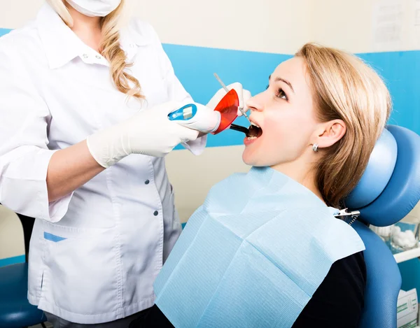 The reception was at the female dentist. Doctor examines the oral cavity on tooth decay. Caries protection. Tooth decay treatment. Dentist working with dental polymerization lamp in oral cavity — Stock Photo, Image