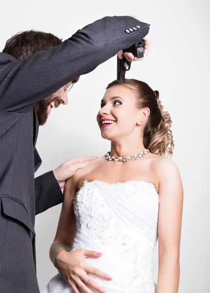 Bela noiva com penteado de casamento de moda. Noivo barbudo com uma arma apontada à cabeça da noiva. casamentos desiguais — Fotografia de Stock