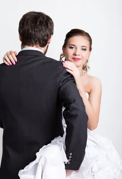 Όμορφη νύφη με το χτένισμα του γάμου μόδας. Κοντινό-up πορτραίτο της νεαρής πανέμορφης νύφης. ο γαμπρός είναι με την πλάτη του, αγκαλιάζοντας τη νύφη γαμπρό — Φωτογραφία Αρχείου
