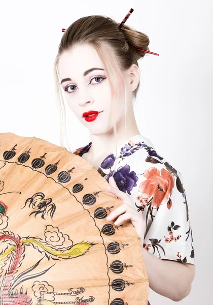 beautiful girl dressed as a geisha girl holding a Chinese umbrella. Geisha makeup and hair dressed in a kimono. The concept of traditional Japanese values