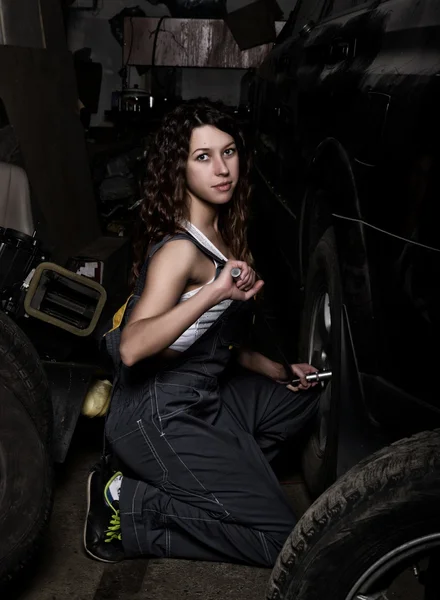 Sexy girl mechanic sitting on a tire holding a wrench in his hand. colorless life concept — Stock fotografie