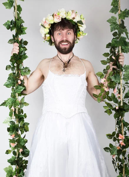 bearded man in a womans wedding dress on her naked body, clinging to the vine. grimacing and funny. on his head a wreath of flowers. funny bearded bride