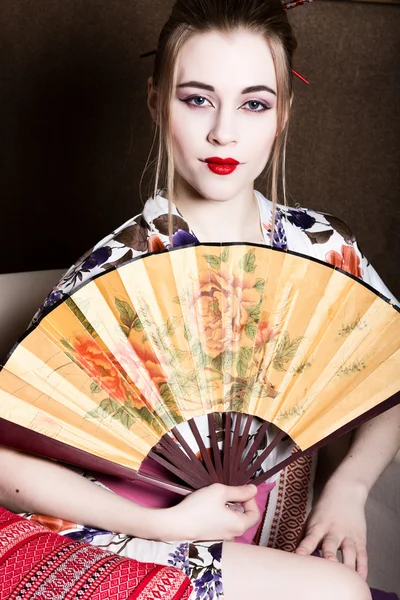 Schönes Mädchen als Geisha gekleidet, hält sie einen chinesischen Fächer. Geisha Make-up und Haare in einem Kimono gekleidet. das Konzept traditioneller japanischer Werte — Stockfoto