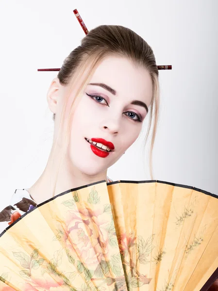 Menina bonita vestida como uma gueixa, ela detém um fã chinês. Maquiagem de gueixa e cabelo vestido com um quimono. O conceito de valores tradicionais japoneses — Fotografia de Stock