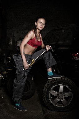 sexy girl mechanic sitting on a tire holding a wrench in his hand. colorless life concept
