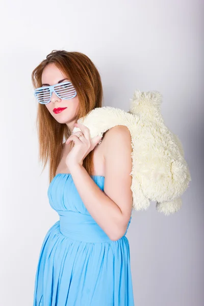 Chica en un vestido azul y gafas de sol en el estilo de discoteca, abrazando a un oso de peluche en los mismos vasos — Foto de Stock