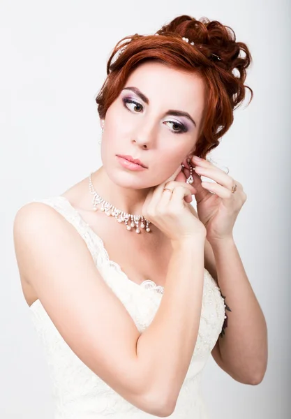 Schöne Braut in einem Hochzeitskleid mit Hochzeits-Make-up und Frisur. Braut steckt Ohrringe ins Ohr — Stockfoto