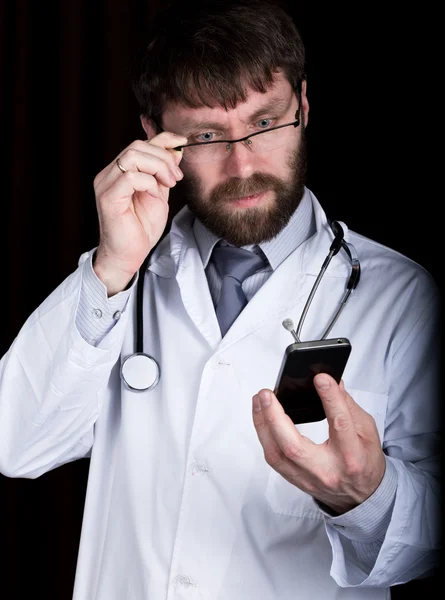 Dr. szakállas manin egy fehér orvosi köpenyt, a nyakán, sztetoszkóp, érzelmileg beszél telefonon — Stock Fotó