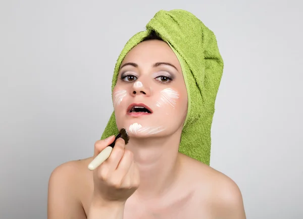 Piękna młoda kobieta ubrana w ręcznik kąpielowy sprawia, że kosmetyk maski na twarzy. piękno przemysł i domu skóry opieki koncepcja — Zdjęcie stockowe