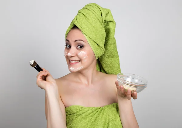 Gyönyörű fiatal nő öltözve egy törölköző teszi a kozmetikai maszk az arcon. szépség ipar és hazai bőr care koncepciót — Stock Fotó