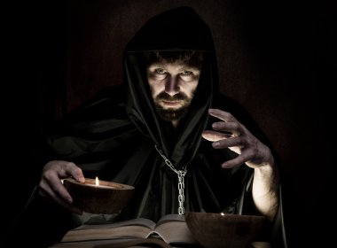 karanlık bir arka plan üzerinde mum ışığında kalın antik kitaptan büyü büyücü çevirir