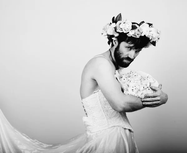 bearded man in a womans wedding dress on her naked body, holding a flower. on his head a wreath of flowers. funny bearded bride, black and white