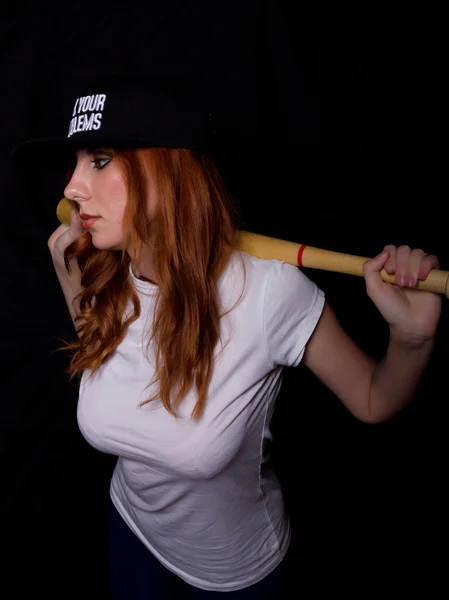 Giovane ragazza adolescente in camicia bianca e cappello nero, in posa con una mazza da baseball. gioco di luci e ombre — Foto Stock