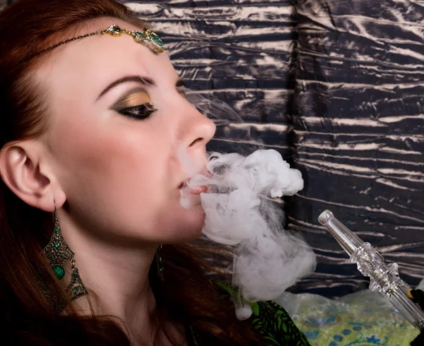 Close-up portrait of a elegant young redhead woman, with oriental make-up and shawl over her head bright red lips, she smokes a hookah — Stock Photo, Image