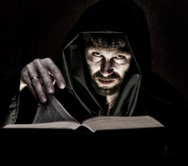 karanlık bir arka plan üzerinde mum ışığında kalın antik kitaptan büyü büyücü çevirir