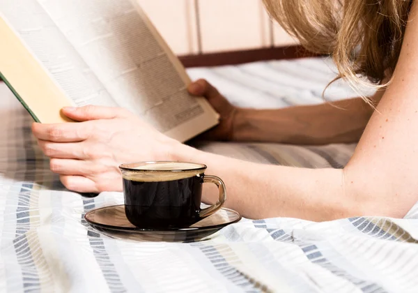 Hermosa mujer leyendo un libro grueso acostado en la cama, taza de café de primer plano — Foto de Stock