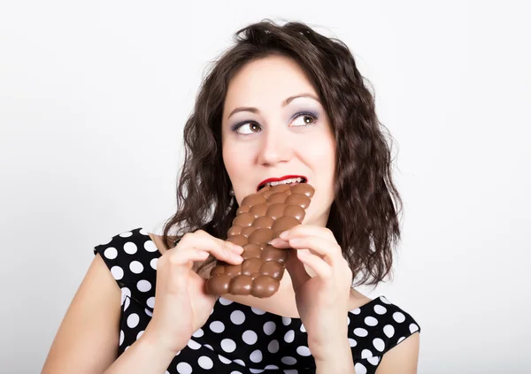 Hermosa mujer joven comiendo una barra de chocolate, lleva un vestido con lunares — Foto de Stock