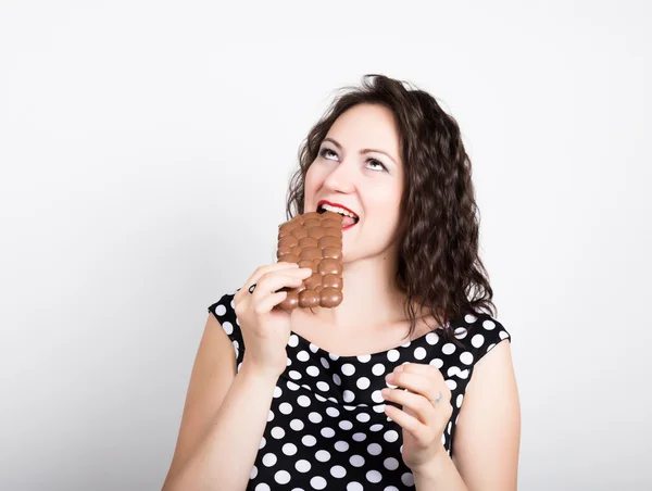 Hermosa mujer joven comiendo una barra de chocolate, lleva un vestido con lunares — Foto de Stock