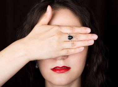 Yakın çekim kadın siyah bir arka plan üzerinde doğrudan fotoğraf makinesine benziyor. Elini gözleriyle kapsayan kadın gülüyor. farklı duygular ifade eder