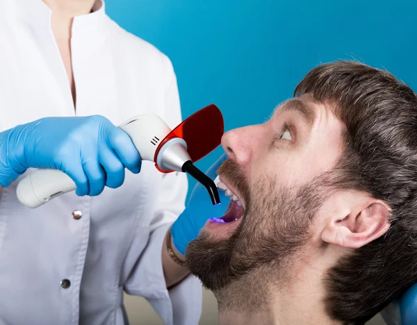 O médico examina a cavidade oral na cárie dentária. Protecção de cáries. Tratamento da cárie dentária. Dentista que trabalha com lâmpada de polimerização dentária na cavidade oral — Fotografia de Stock