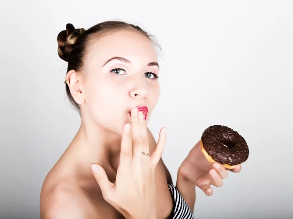 Ung kvinna i ljusa makeup äta en välsmakande donut med glasyr. Funny glad kvinna med godis, dessert. bantning koncept. skräpmat. tjej slickar sina fingrar — Stockfoto