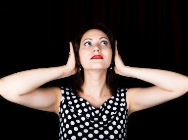 Yakın çekim kadın siyah bir arka plan üzerinde doğrudan fotoğraf makinesine benziyor. gülen kadın onun kulaklarını elleriyle kapsar. farklı duygular ifade eder