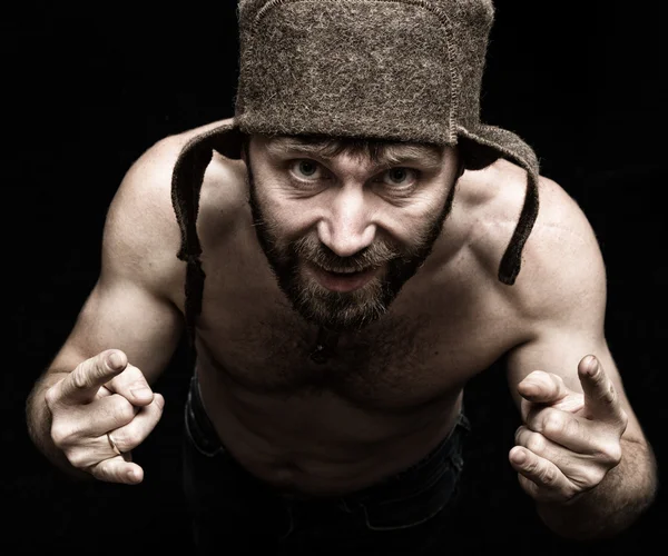 O retrato escuro do homem barbudo sinistro maligno assustador com o sorriso, faz vários sinais de mãos e expressa emoções diferentes. estranho russo homem com um torso nu e um chapéu de lã — Fotografia de Stock