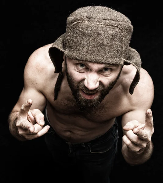 Temný portrét strašidelného zlého vousatého muže s úškleby, dává různým rukama znamení a vyjadřuje různé emoce. podivný ruský muž s nahou trupem a vlněné čapkou — Stock fotografie