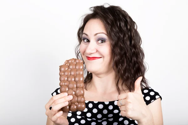 Hermosa mujer joven comiendo una barra de chocolate, lleva un vestido con lunares. expresa diferentes emociones — Foto de Stock