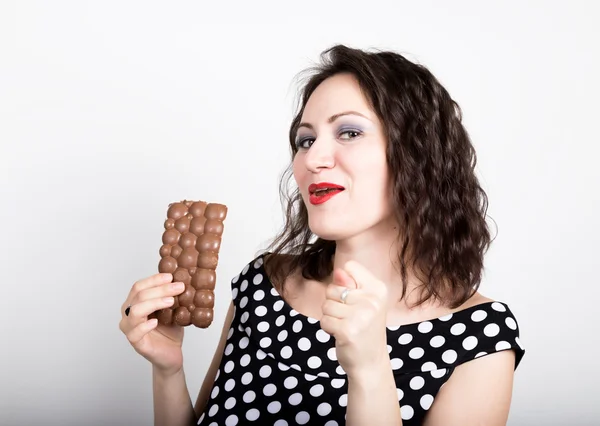 Hermosa mujer joven comiendo una barra de chocolate, lleva un vestido con lunares. expresa diferentes emociones — Foto de Stock