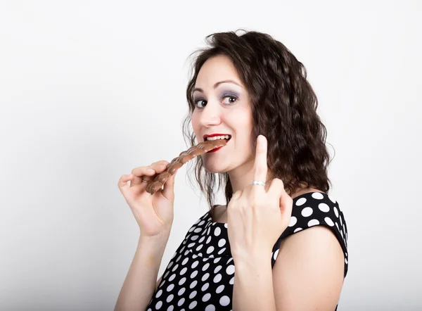 Hermosa mujer joven comiendo una barra de chocolate, lleva un vestido con lunares. expresa diferentes emociones — Foto de Stock