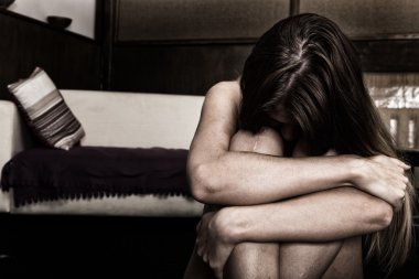 Yatağın yanında boş bir odada yalnız oturan üzgün kadın. Aile içi şiddet
