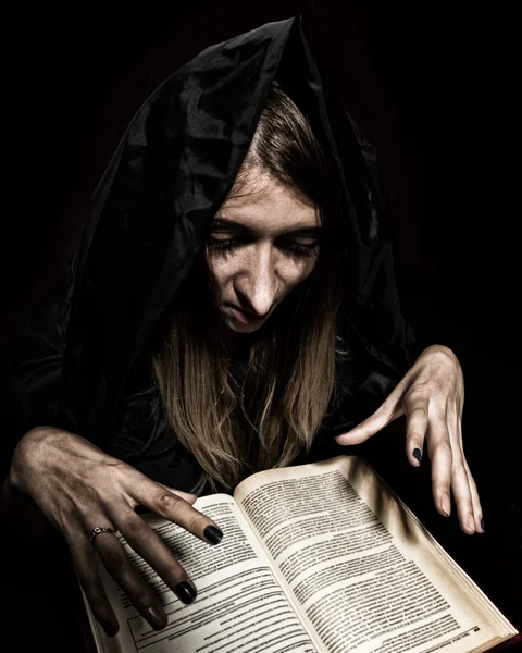 Красивая ведьма накладывает заклинания из толстой древней книги при свечах на темном фоне — стоковое фото