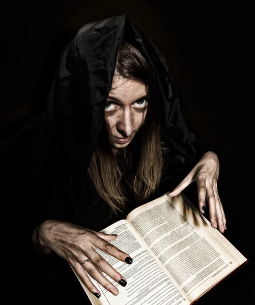 Bonita bruja lanza hechizos de grueso libro antiguo a la luz de las velas sobre un fondo oscuro — Foto de Stock