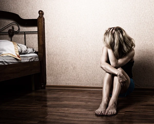 Triste mujer sentada sola en una habitación vacía junto a la cama. violencia doméstica —  Fotos de Stock