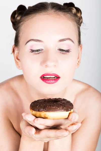 Девушка в ярком макияже ест вкусный пончик с глазурью. Смешная радостная женщина со сладостями, десертом. Концепция диеты. фастфуд. Девушка с нежностью смотрит на пончик — стоковое фото