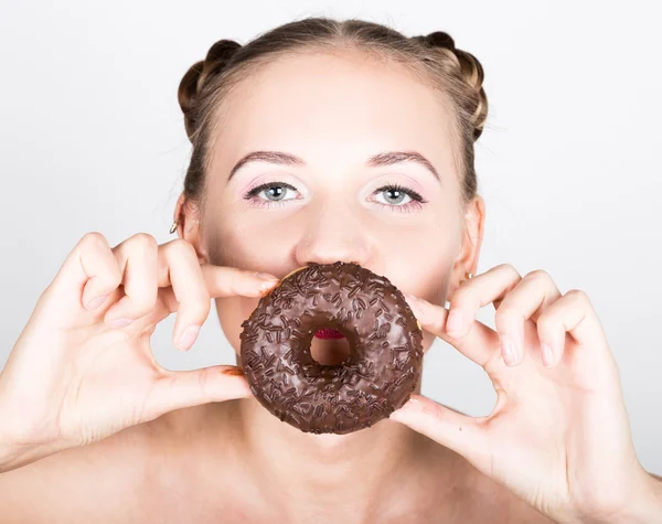 Κορίτσι στο λαμπερό μακιγιάζ που τρώει ένα νόστιμο ντόνατ με γλάσο. Αστεία γυναίκα χαρούμενη γλυκά, επιδόρπιο. δίαιτα έννοια. Πρόχειρο φαγητό. Κοιτάζοντας μέσα από την τρύπα — Φωτογραφία Αρχείου